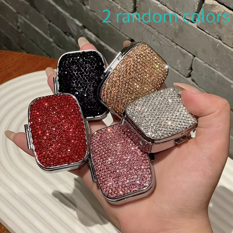 Four glittery compact mirrors in different colors held by a hand against a brick wall.